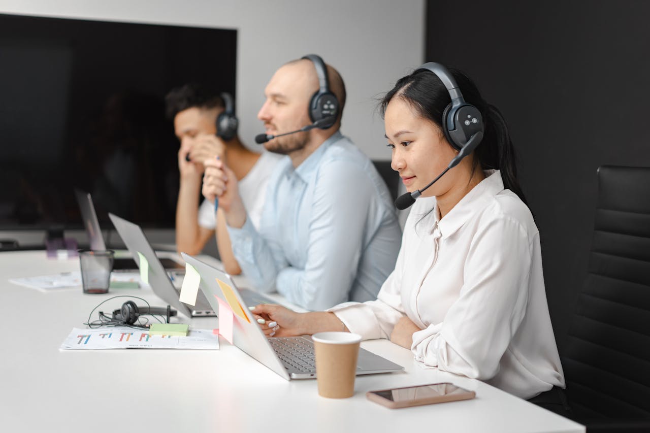 Call center agents wearing headsets working on laptops at a customer support team meeting.